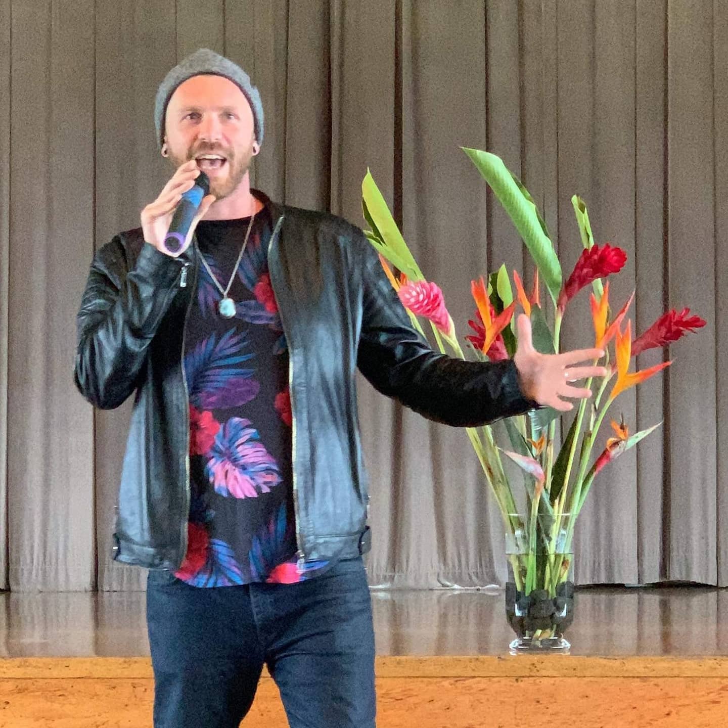 Tala Sage speaking on a stage beside tropical flowers