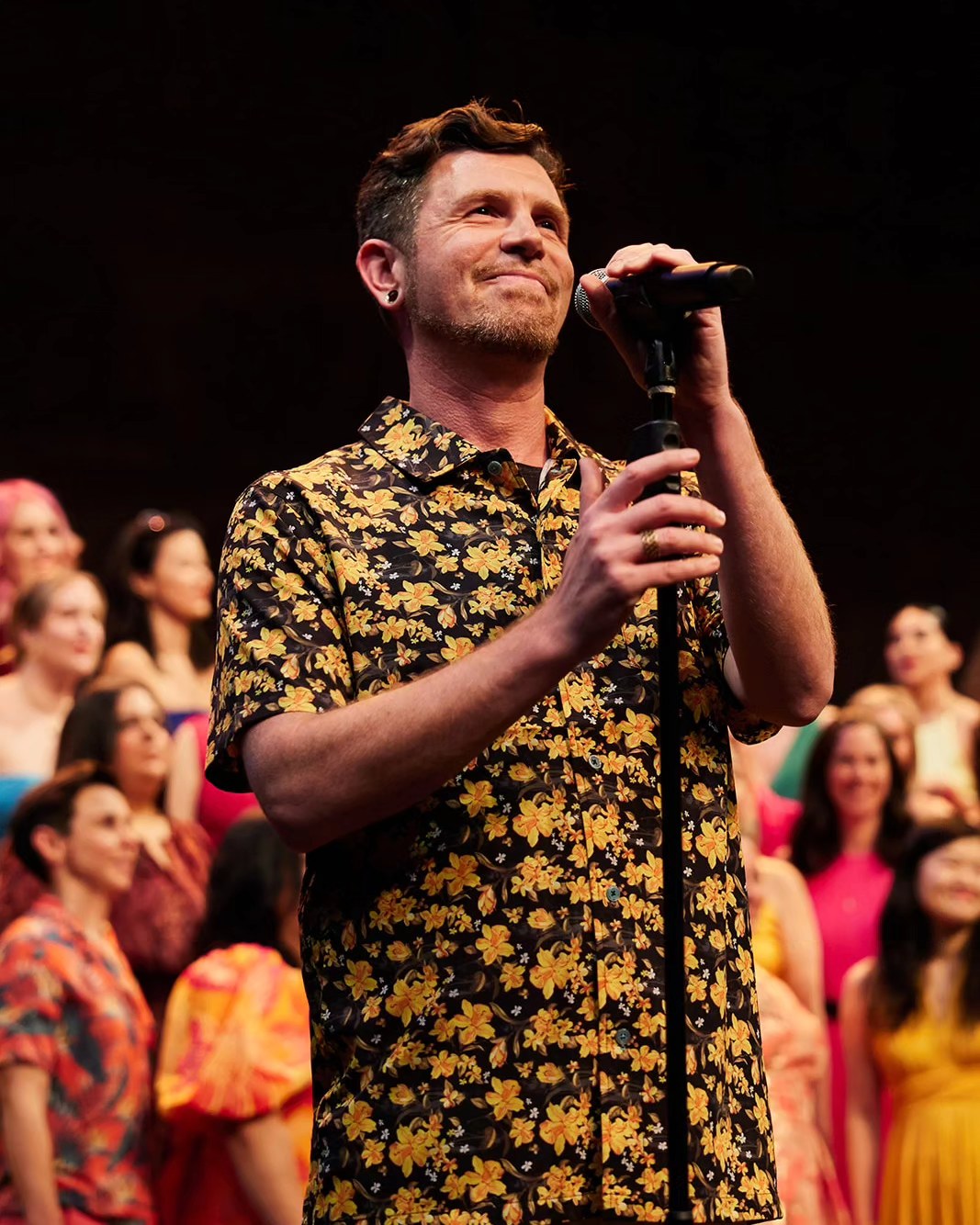 Tala Sage on stage with a mic stand in front of a full cast